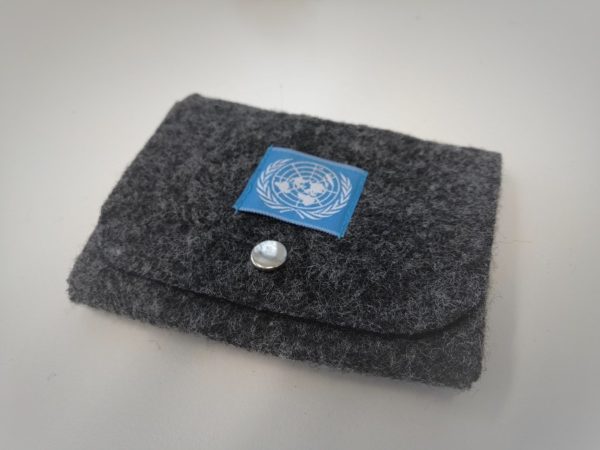Tummanharmaa huovasta tehty rahakukkaro, jonka kannessa metallinen avattava neppari. Kanteen ommeltu kankainen neliö, jossa sinisellä pohjalla YK:n logo